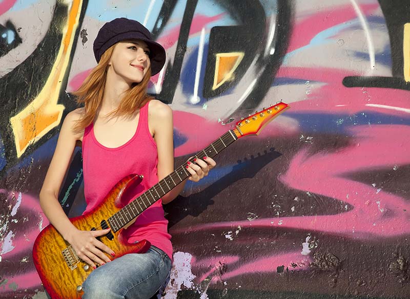 Girl playing guitar next to graffitti wall