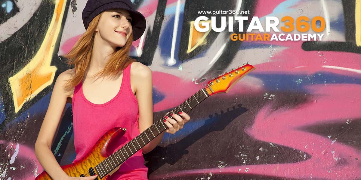 Girl playing guitar next to graffiti wall